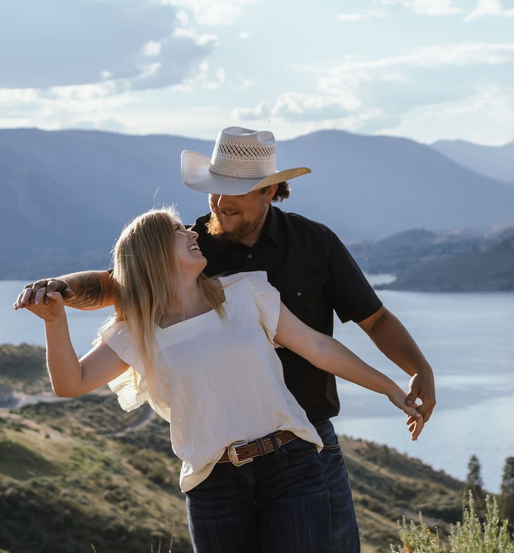 A couple shares a romantic moment together on a mountain overlook with a lake and scenic vista in the background.
