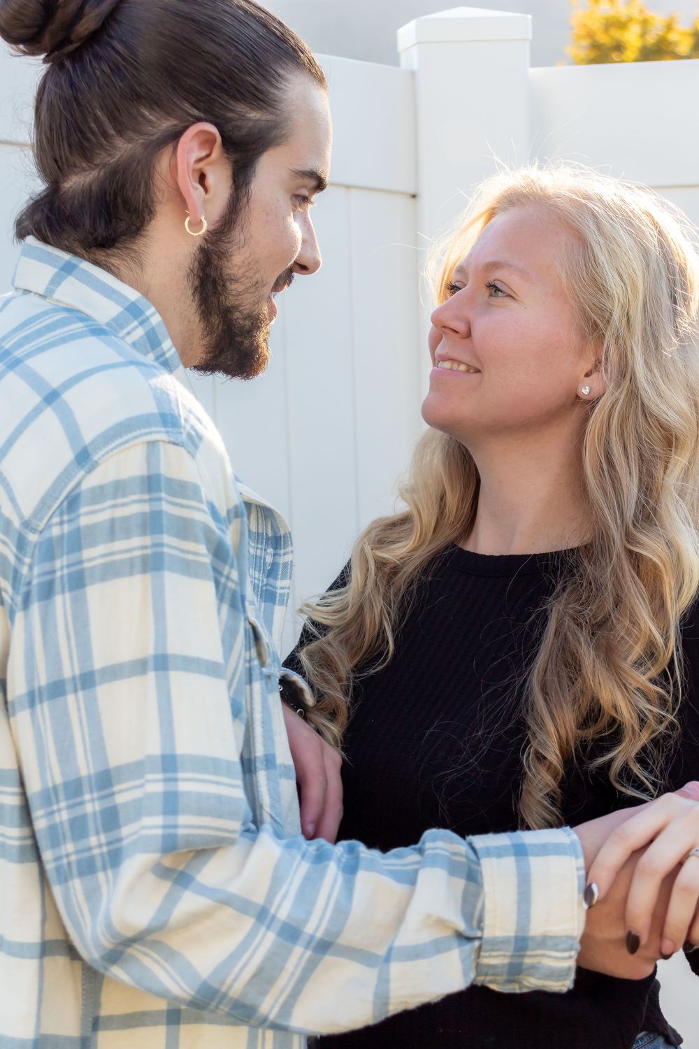 A couple in close conversation outdoors, with one wearing a plaid shirt and the other in a black top.