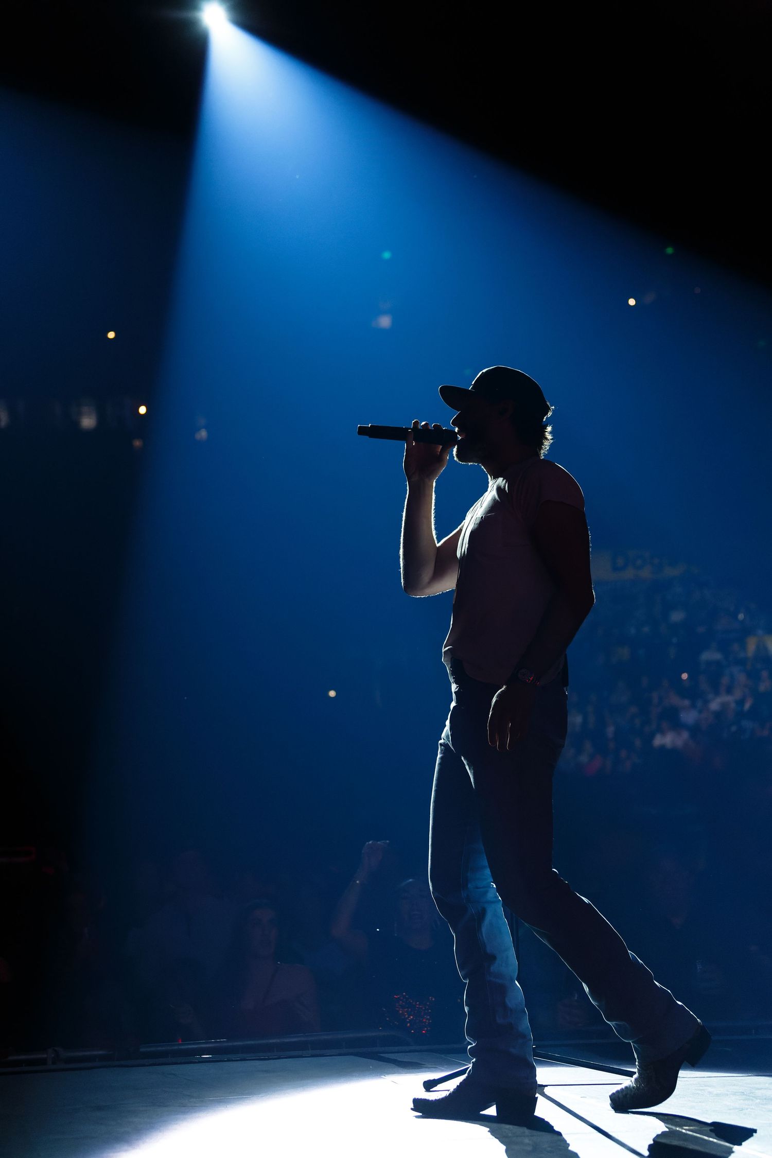 Silhouetted performer Chase Rice singing on stage at Bridgestone Arena under dramatic blue spotlight.