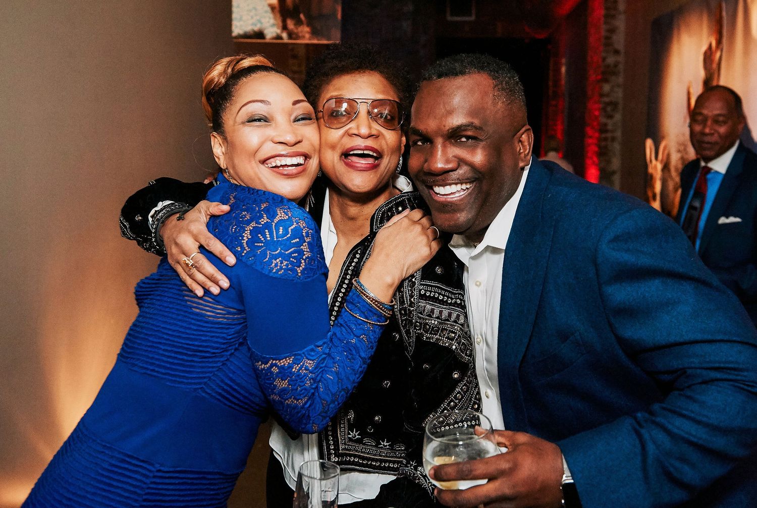 Three friends laugh and pose together at a festive evening party in colorful outfits.