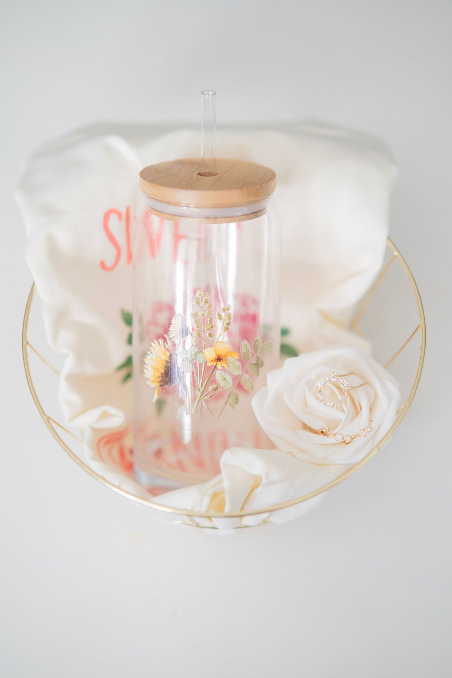 Floral glass tumbler with bamboo lid and straw styled with white rose on gold decorative tray.