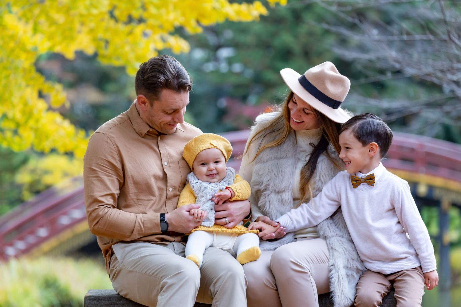 A family enjoys a peaceful moment together on a bench in a garden with yellow flowers blooming in the background.