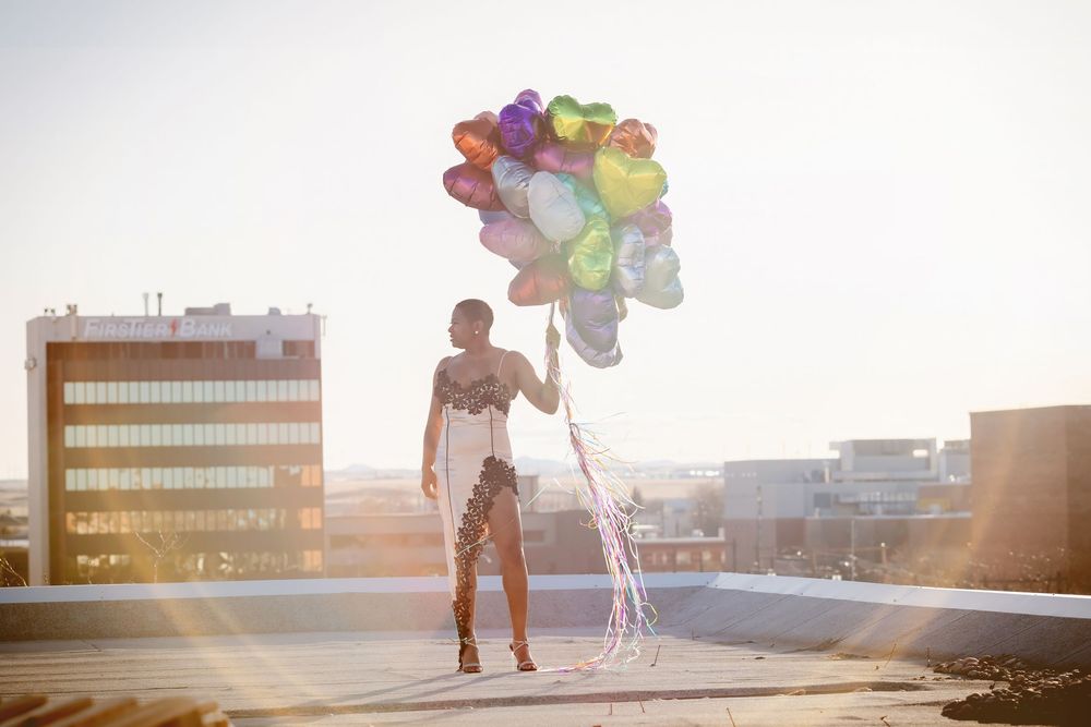 Person running with colorful heart balloons at sunset on an urban rooftop.