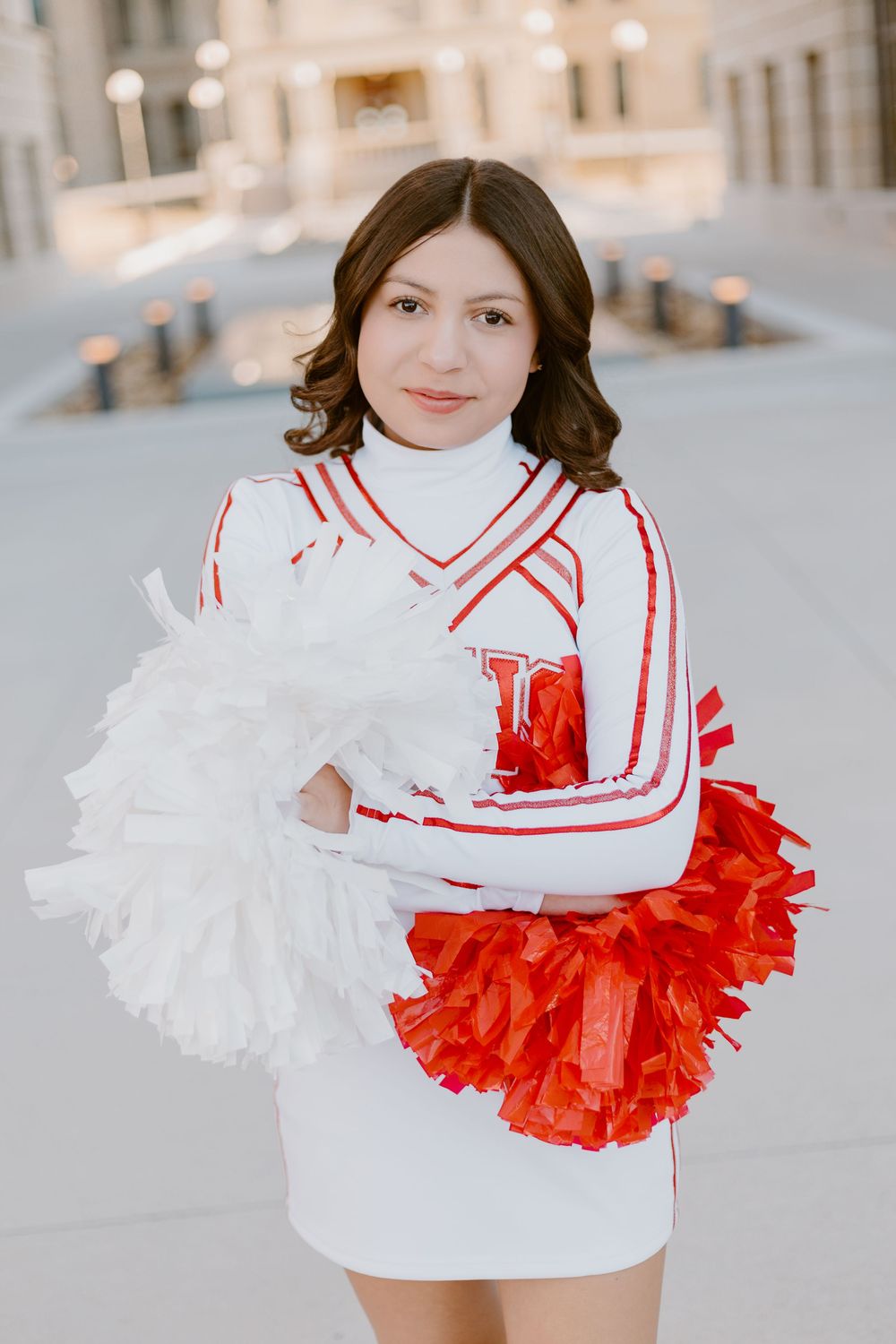 Cheerleader in white uniform with red accents and a ruffled skirt performs outdoors.