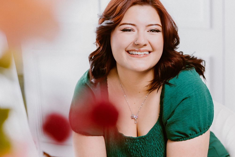 Candid portrait in emerald green dress with blurred red flowers in foreground.