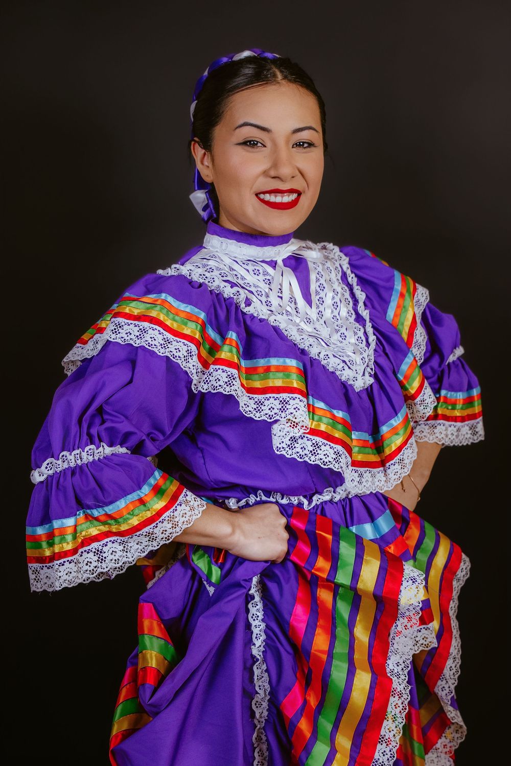 Dancer wearing purple traditional Mexican dress with colorful striped ruffles and white lace.