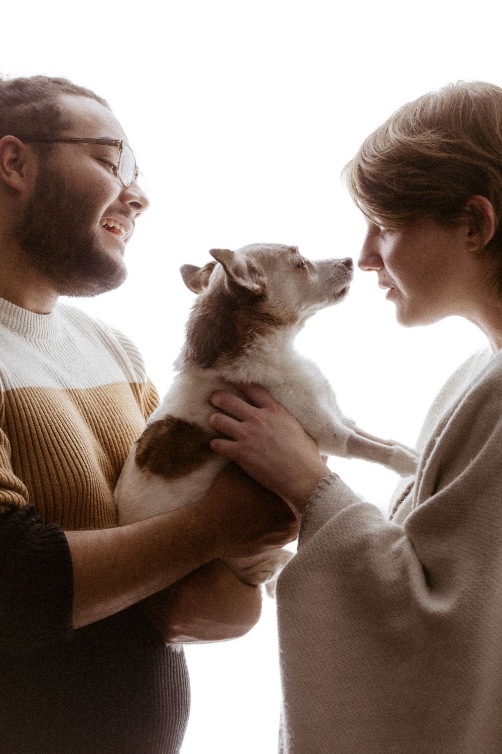 Couple in warm sweaters sharing tender moment with their small white dog.