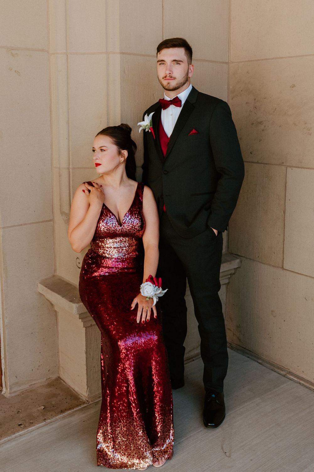 Artistic fashion portraits of couple in red sequin gown and black suit against stone wall.