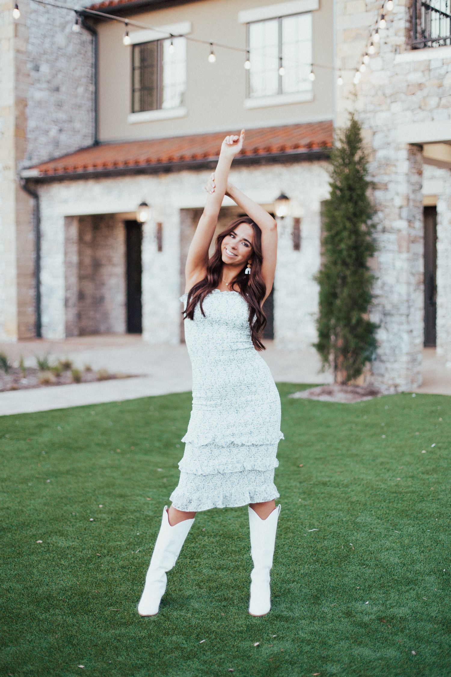 A person in a white dress jumps joyfully on a lawn in front of a stone building.