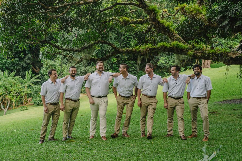 A group wearing matching khaki pants and light colored shirts standing together on a lawn with lush greenery.