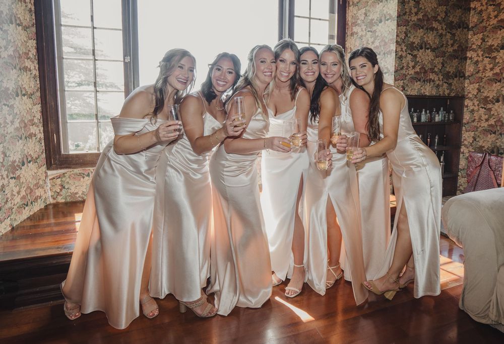 A group wearing matching white satin dresses posing together in an elegant indoor venue.