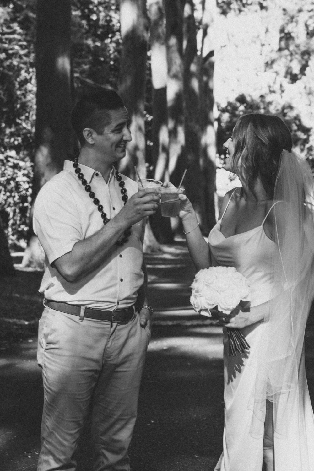A black and white photo of a couple sharing a drink outdoors during a wedding celebration.