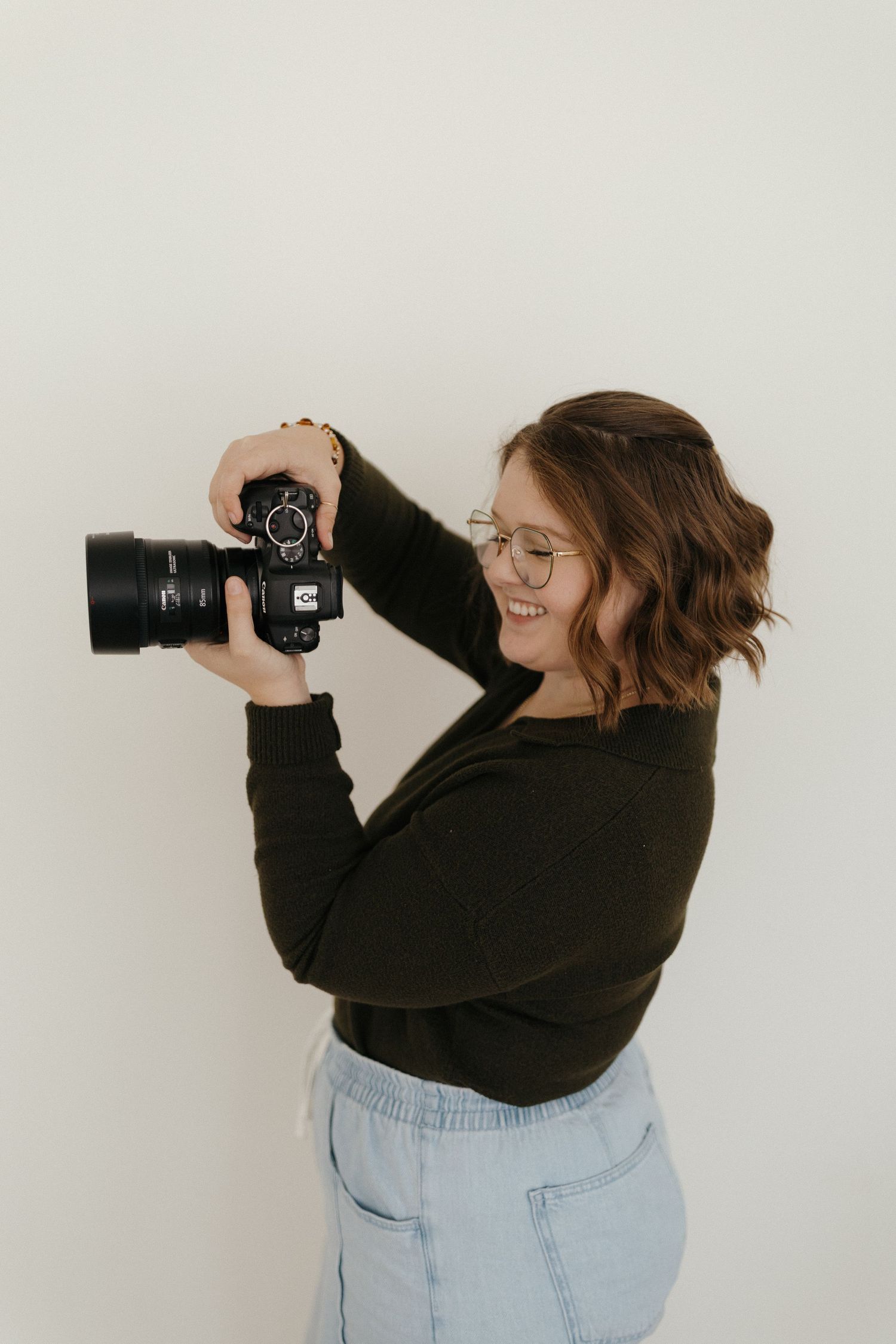 Photographer sitting on hardwood floor wearing white crochet sweater and black pants with camera nearby.