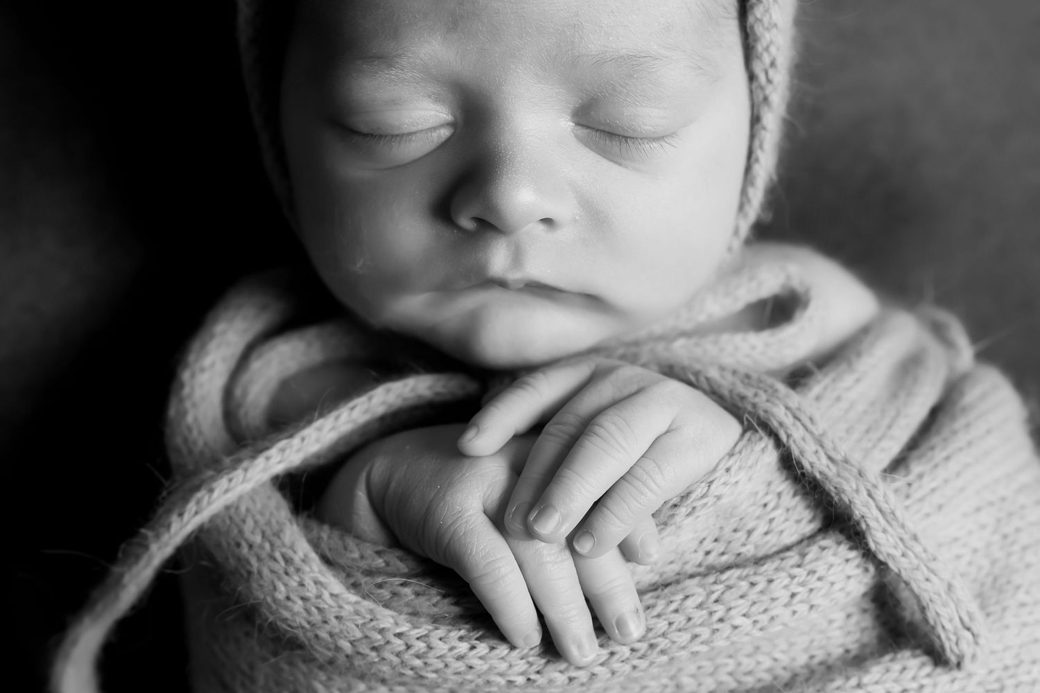 Sweet sleeping newborn baby wrapped in cozy knit blanket captured in intimate black and white portrait.
