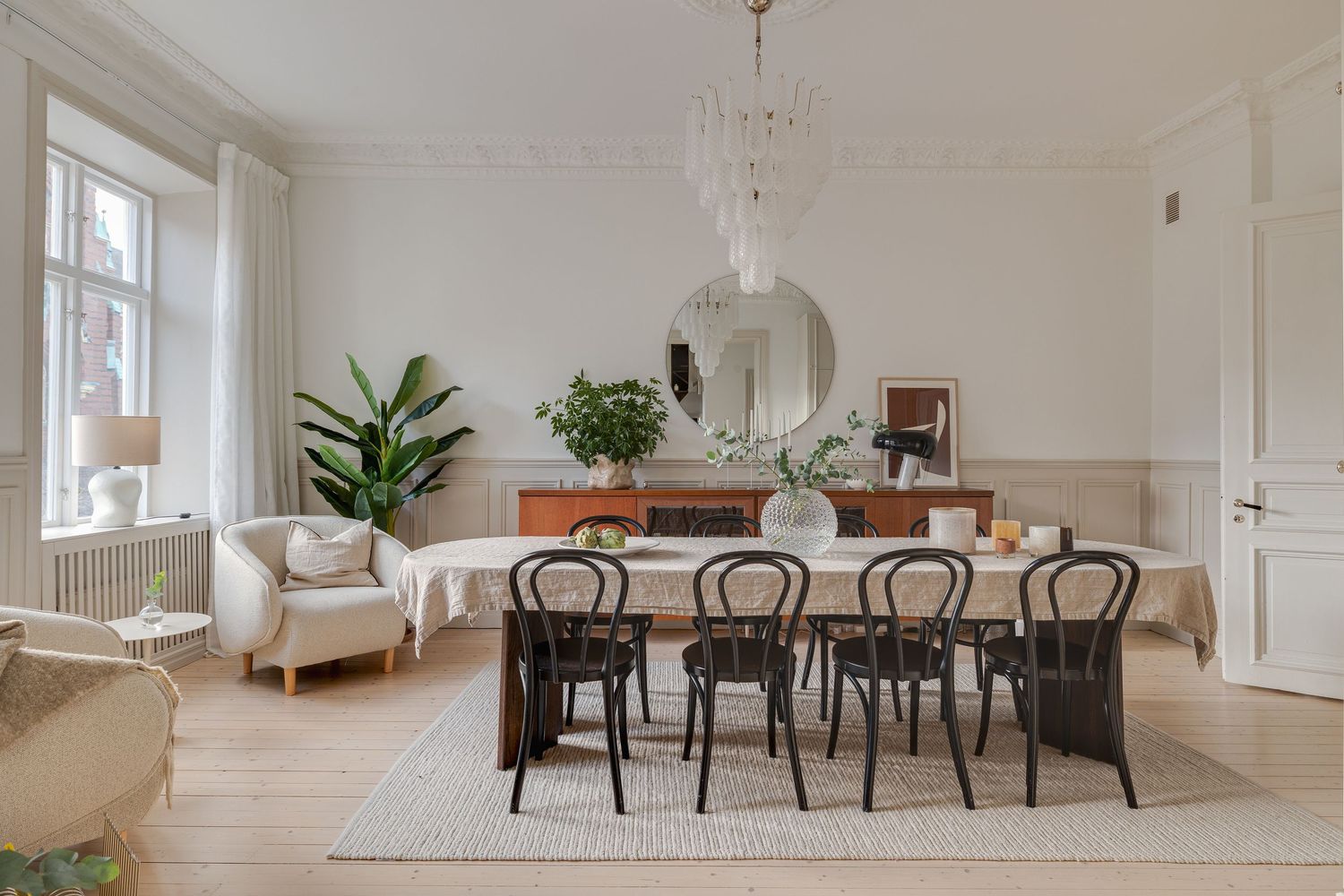Bright Scandinavian dining room with bentwood chairs, wooden table, white walls, and large windows bringing in natural light.