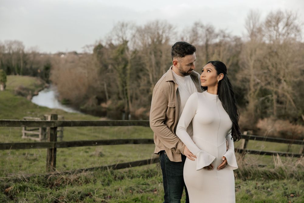 A loving couple stands together on a hillside overlooking a winding river during a romantic outdoor photo session.