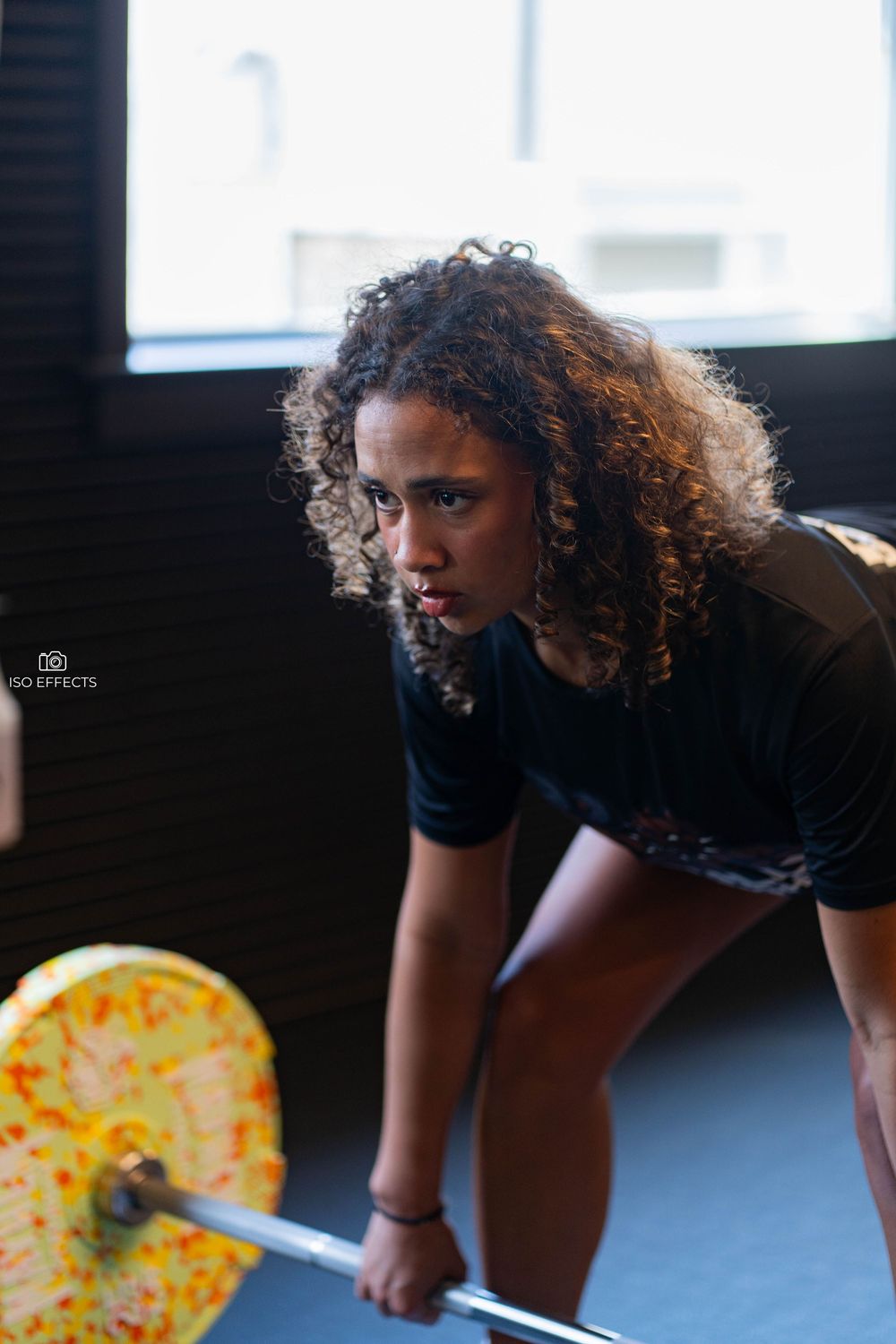 Weightlifter in dark workout gear grips colorful barbell plates in dramatic gym lighting.