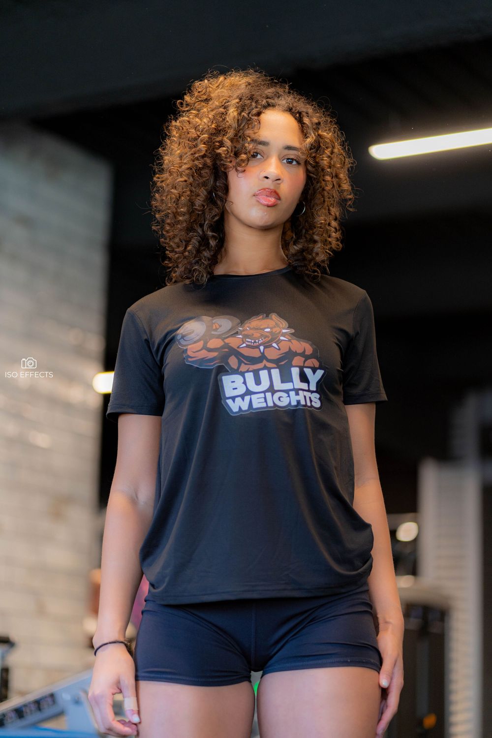 Fitness photo showing Bully Weights t-shirt and navy workout shorts against brick wall backdrop.