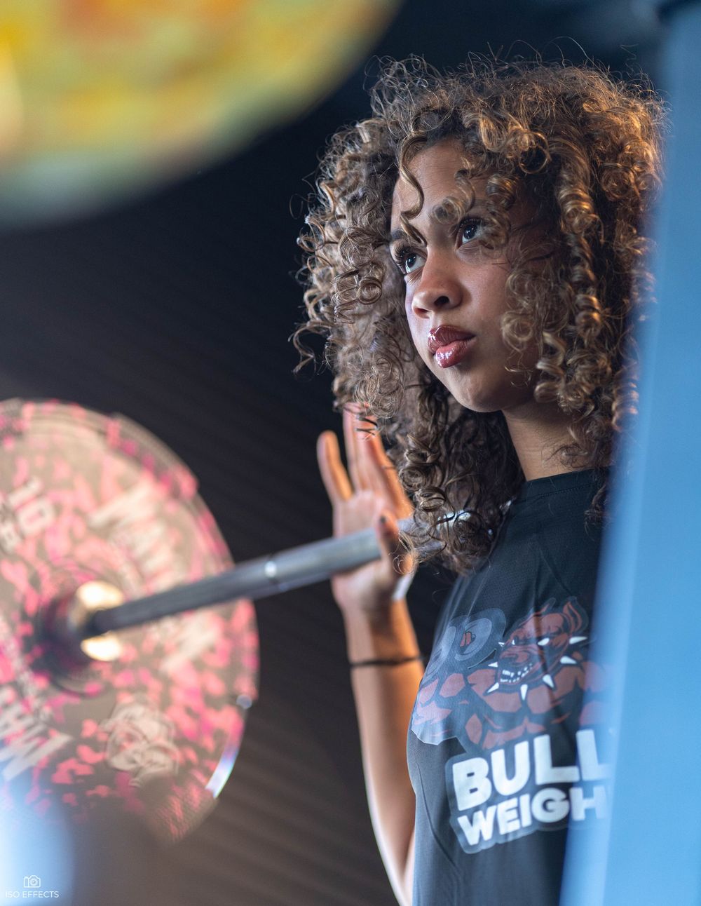 Singer in a black t-shirt with curly hair performs on stage with microphone and dramatic lighting.