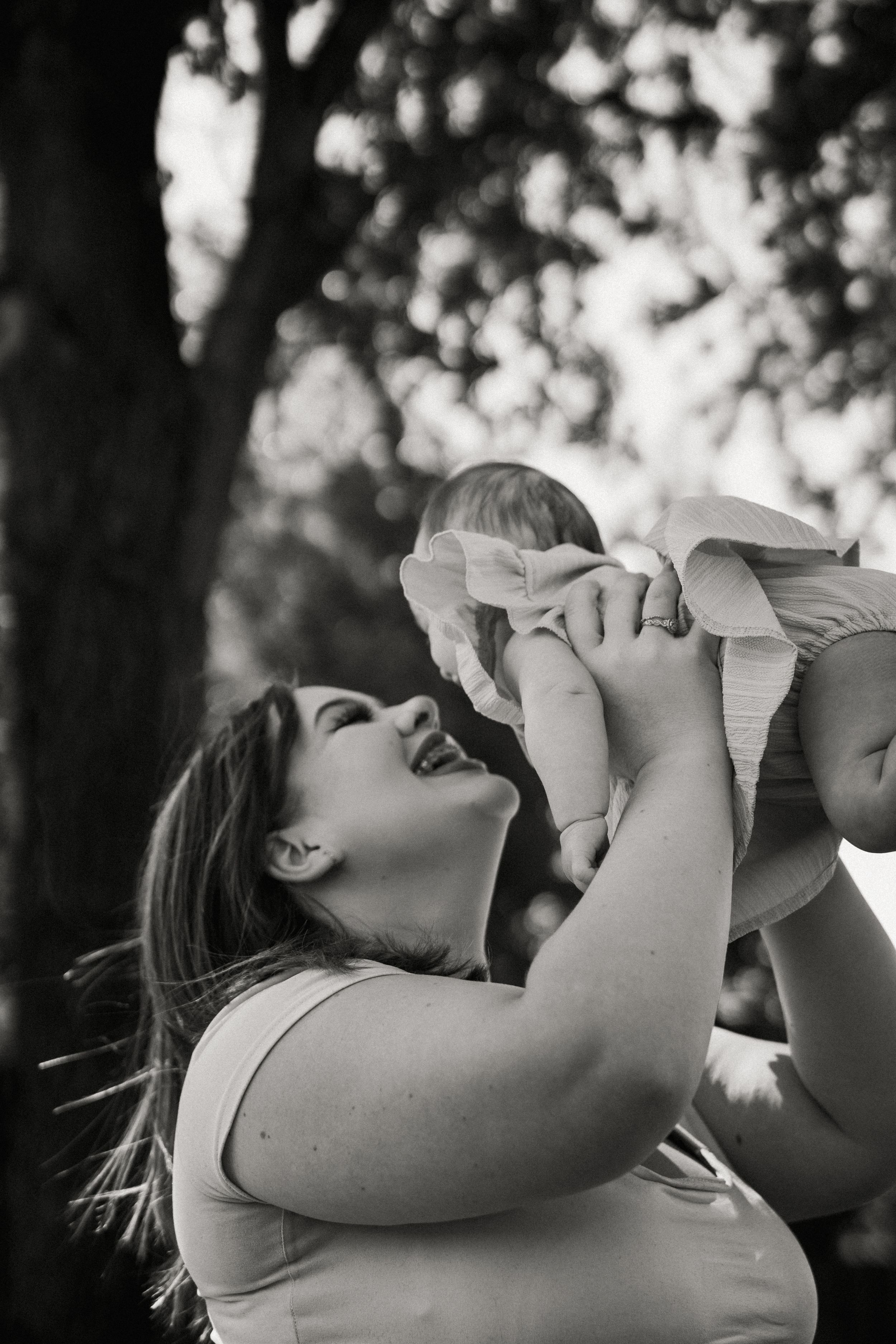 A joyful black and white photo capturing an intimate moment of affection between a woman and baby outdoors.
