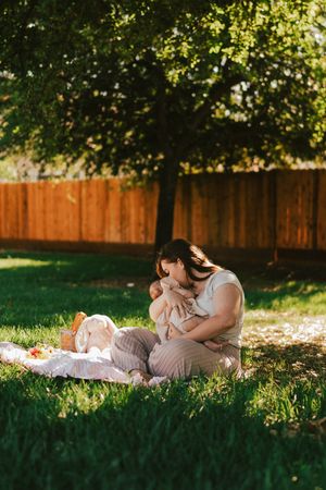 A tender moment shared on a blanket under a tree in a sunlit backyard with a wooden fence.