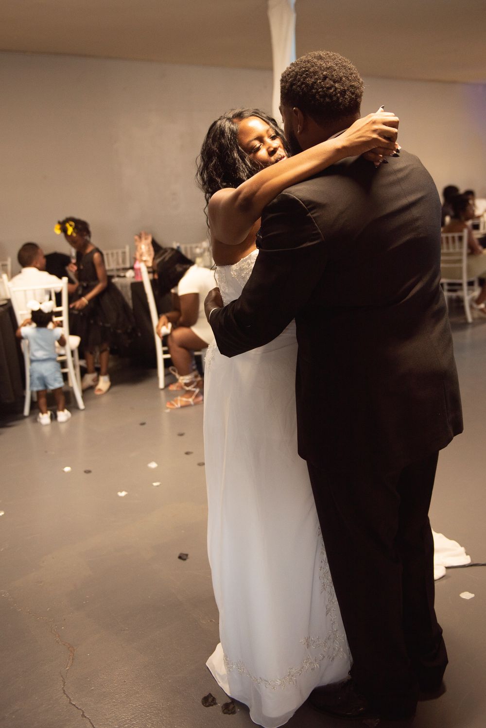 A couple shares their first dance at a wedding reception as guests watch in the background.