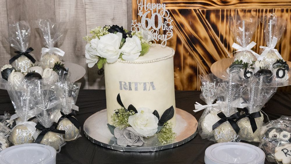 Elegant white wedding cake displayed with champagne flutes and decorative party favors on a mirrored dessert table.