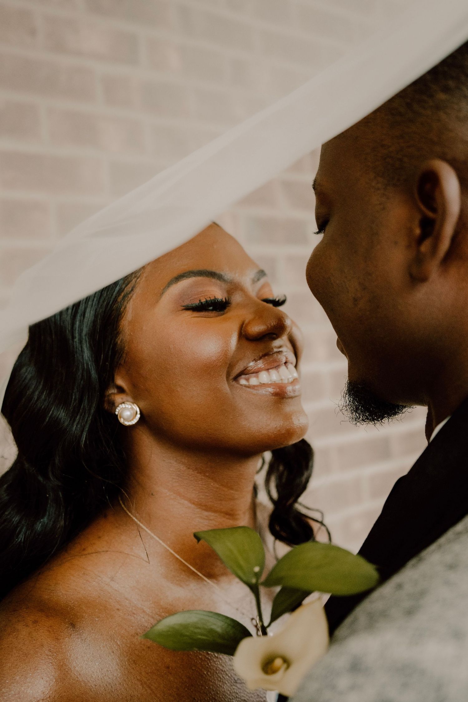 Close-up of joyful couple with white floral accent sharing intimate wedding moment.