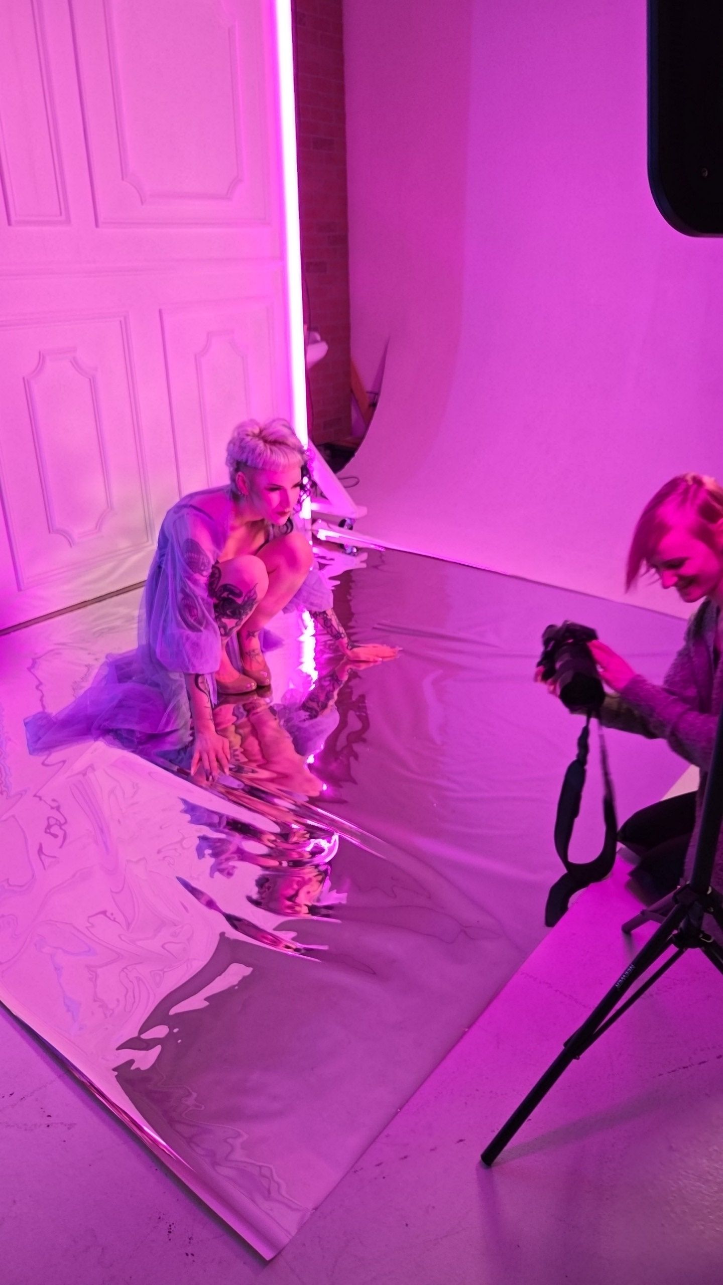 Behind the scenes photo shoot in a studio with pink and purple lighting where a person poses on reflective flooring.