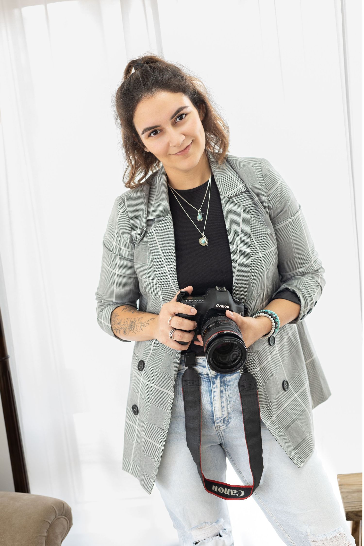 Professional photographer wearing gray blazer and jeans holding camera equipment.