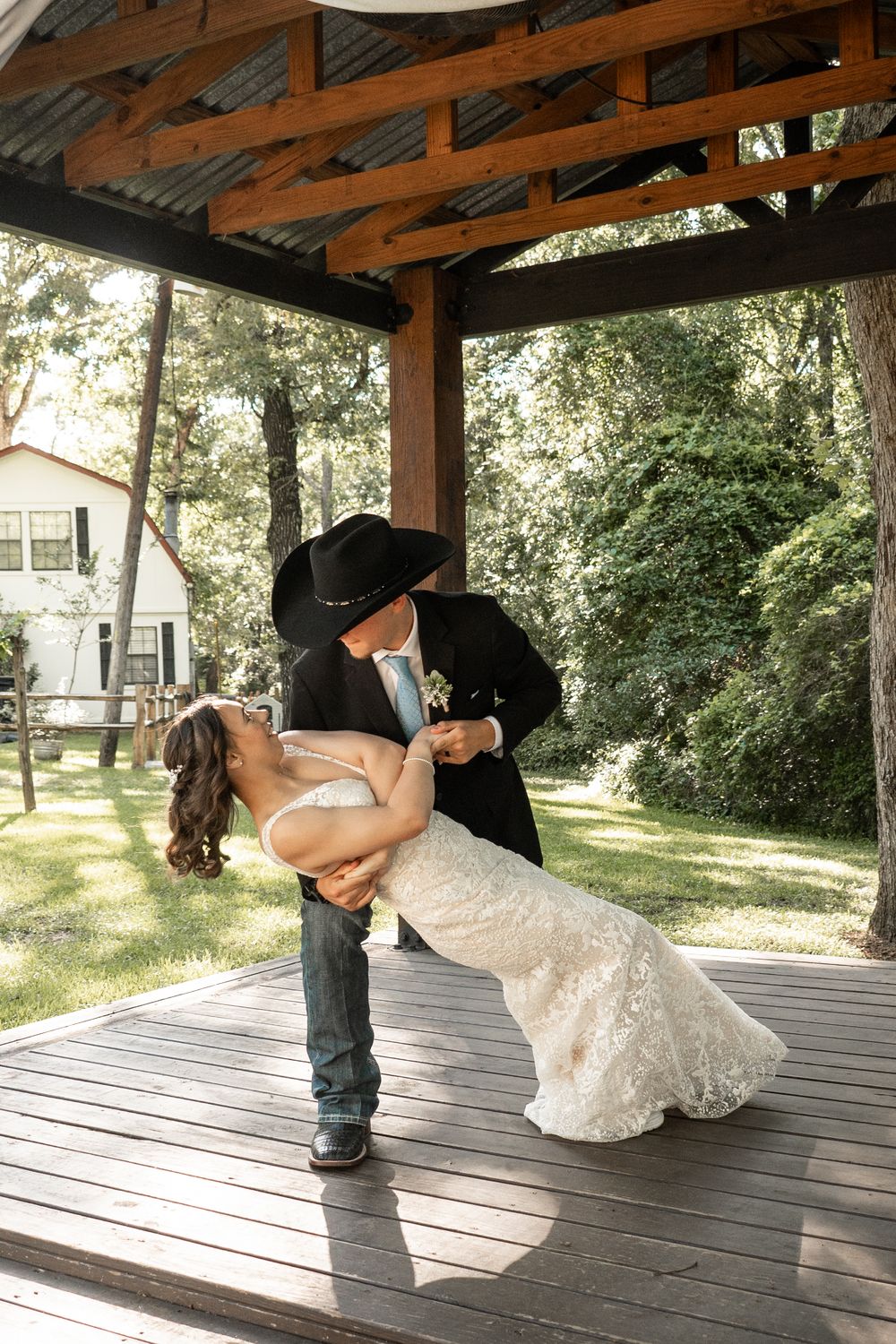 A couple shares a romantic dip kiss under a rustic wooden pavilion during their country wedding celebration.
