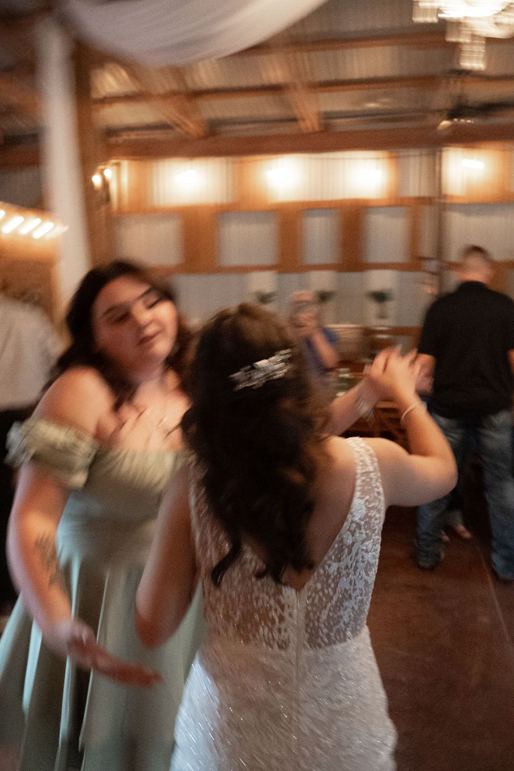 Wedding reception guests dancing and celebrating in a rustic barn venue with string lights overhead.