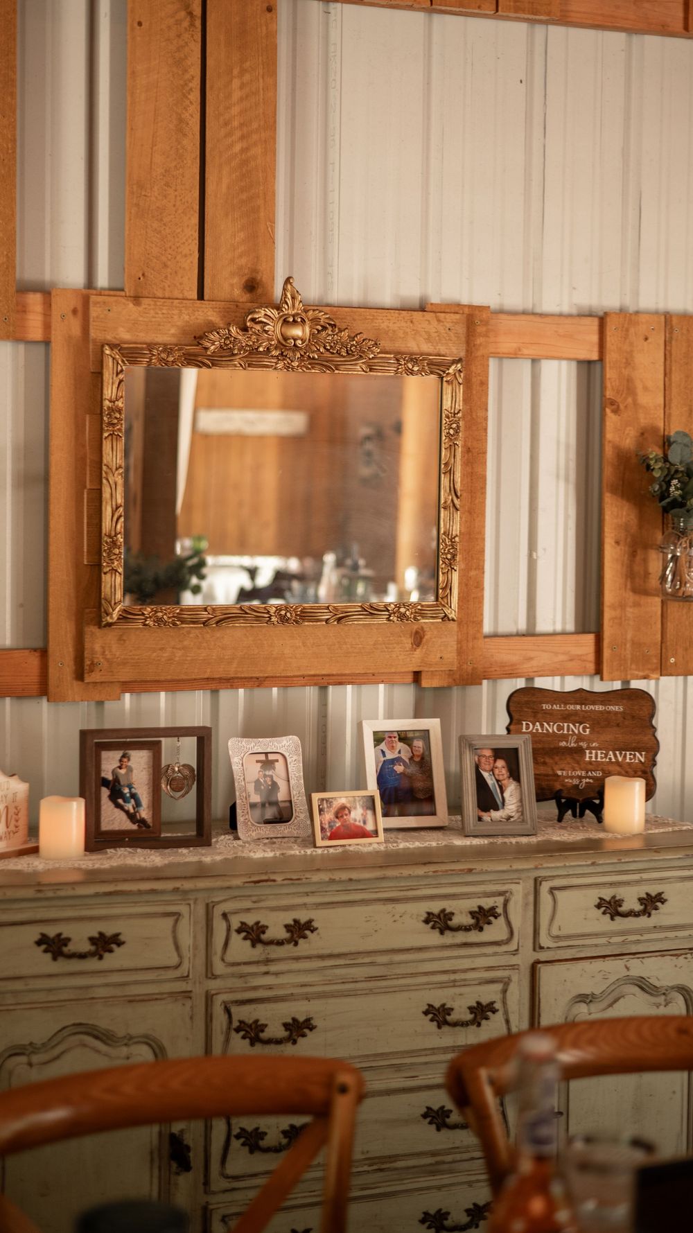 Vintage dresser with ornate gold mirror and framed photos displayed beneath lit candles in rustic wooden interior.