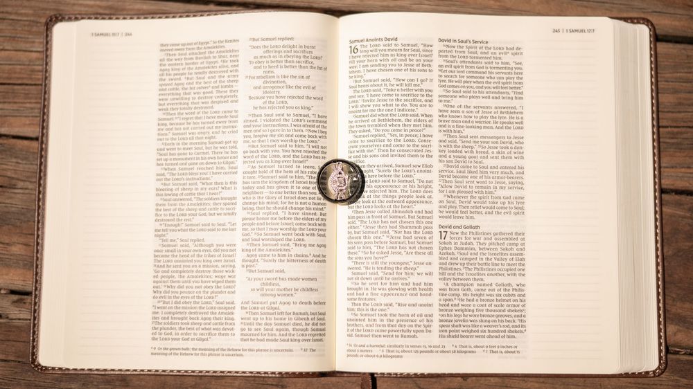 Gold ring rests atop open Bible pages on rustic wooden surface with natural lighting.