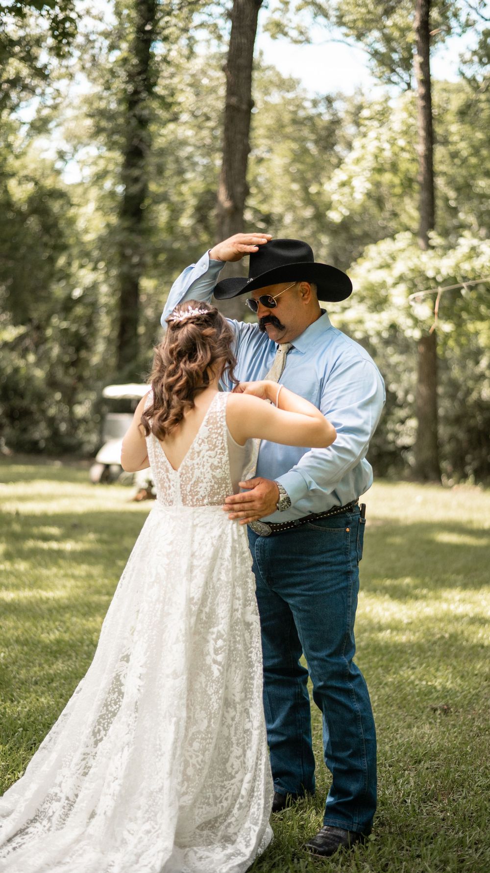 A couple shares their first dance at a rustic outdoor wedding, with the bride in lace and groom in Western attire.