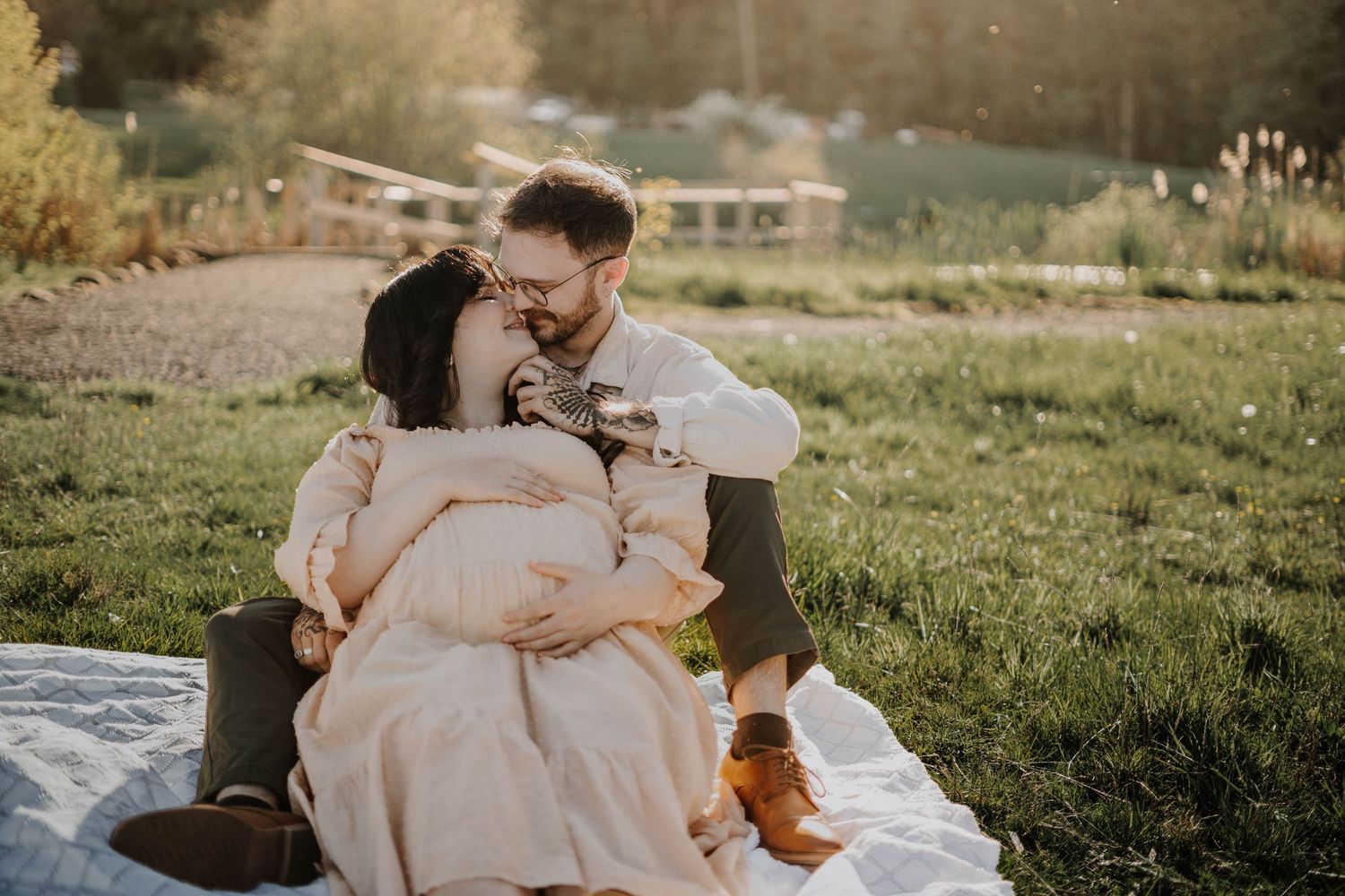Expecting couple laughing together during a romantic sunset maternity session on a blanket outdoors.