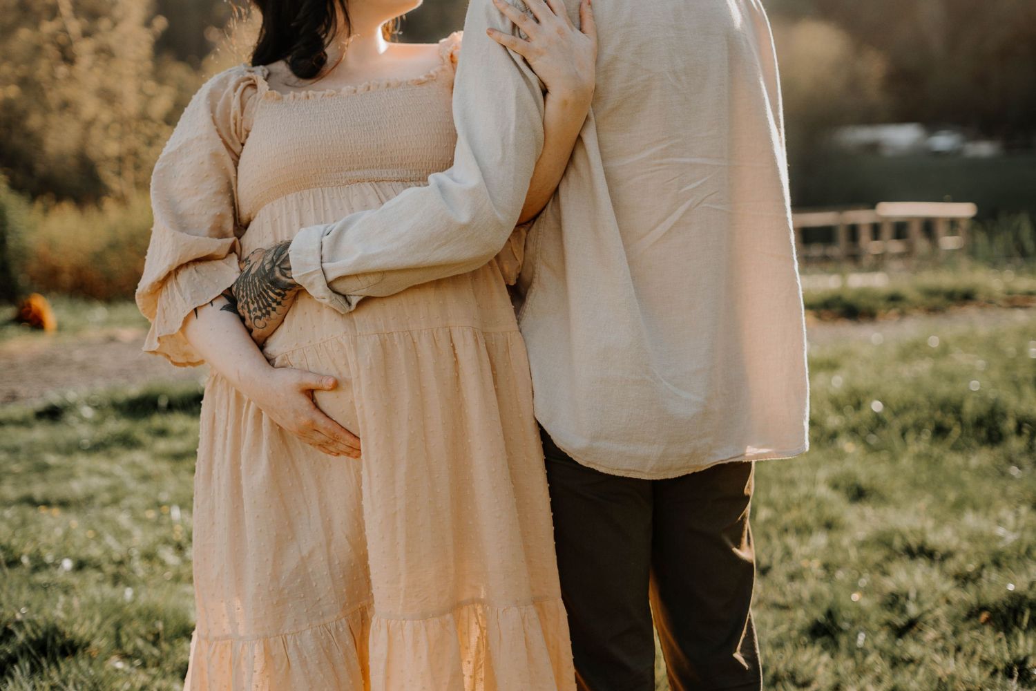 Couple embracing tenderly during a maternity photoshoot in a warm golden hour outdoor setting.