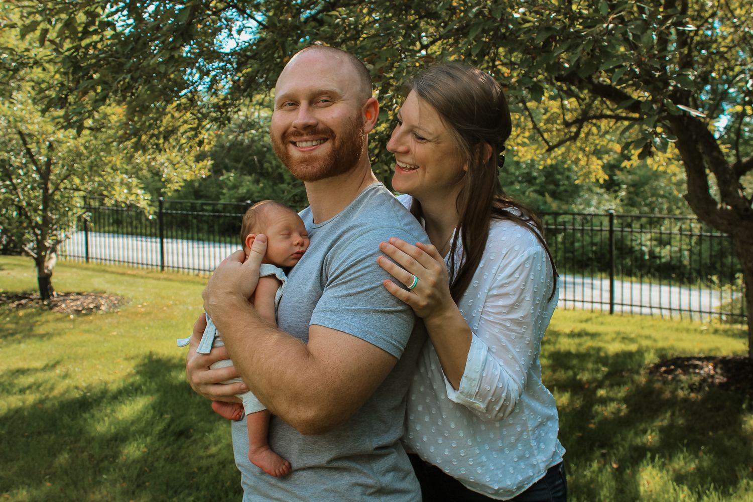 A happy family enjoying a sunny day together in a lush green backyard with a black fence.