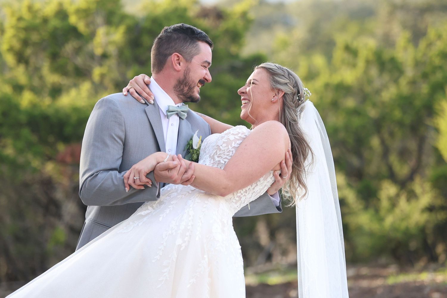 A joyful bride and groom share a romantic dip pose together during an outdoor wedding photoshoot.