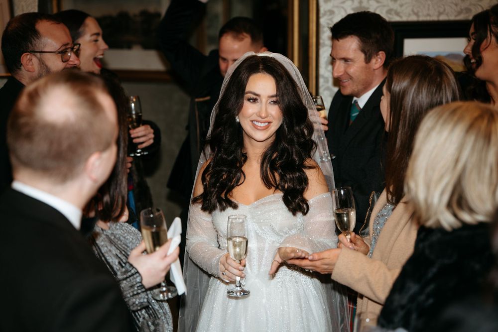 Wedding reception guests mingle and celebrate with drinks in an elegant indoor venue.