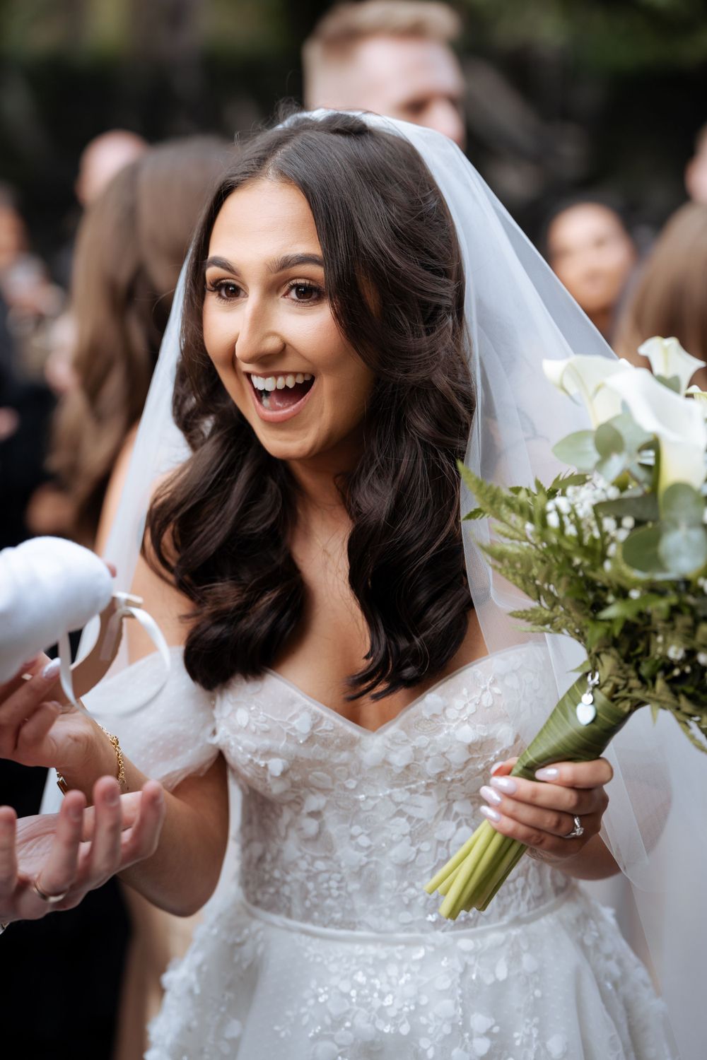 Bride in white lace dress holds a beautiful bouquet of white flowers and greenery.