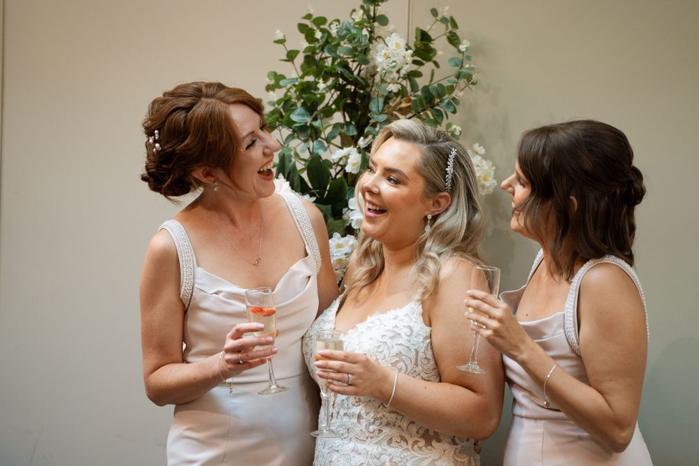 Bridesmaids in coral dresses sharing a candid moment together.