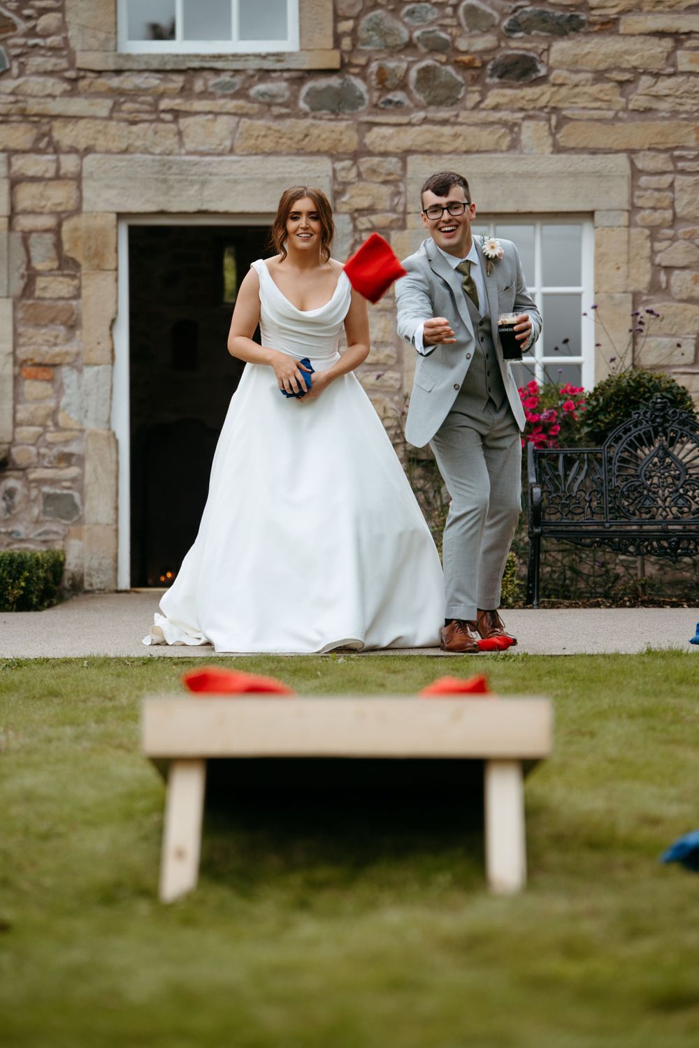 Wedding party playing lawn games outside a rustic stone building.