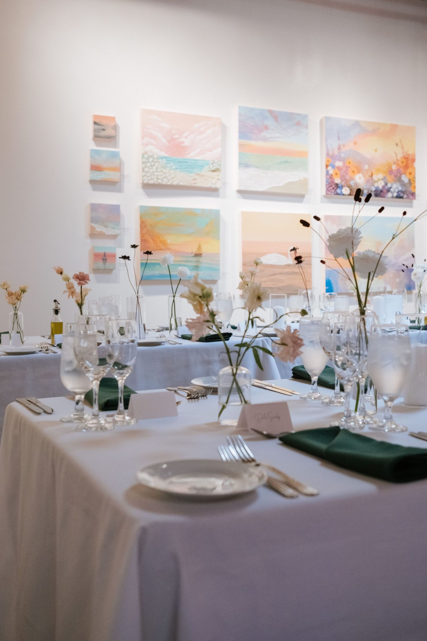 Wedding reception table setting with delicate floral centerpieces and pastel watercolor artwork on the wall.