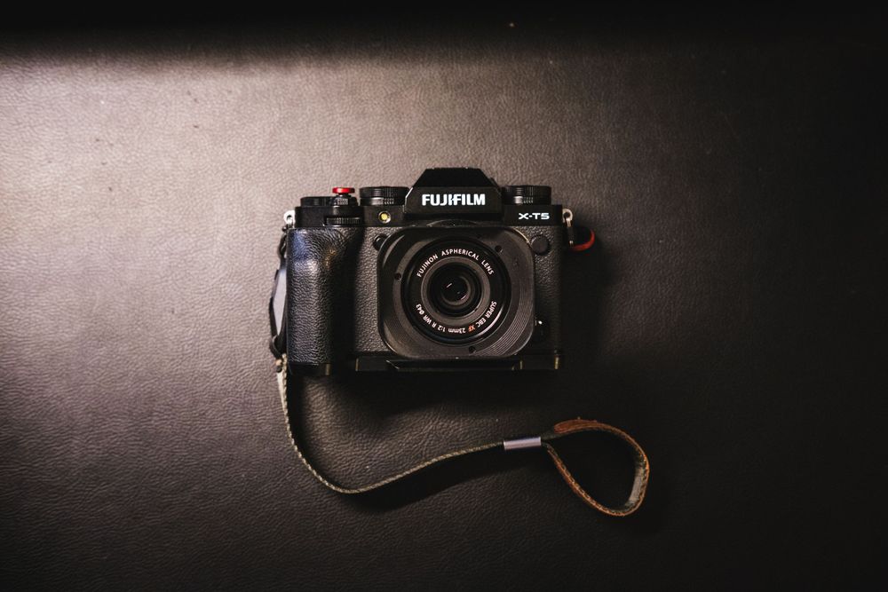 A black fujifilm x-t5 with the Fujifilm 23mm on a black leather background.