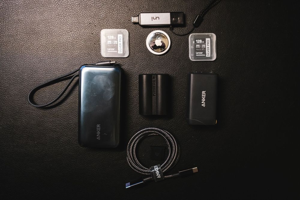 Anker power bank, cord, and wall adapter, lexar sd cards, apple tag, fujifilm camera battery, and a sd card reader on a black backgorund