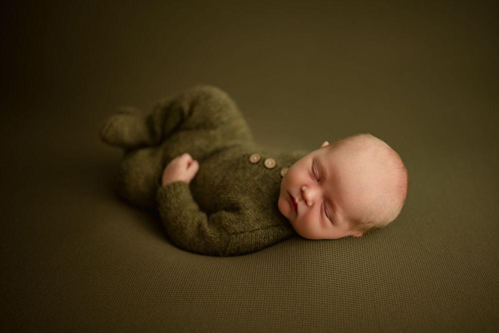 Newborn baby boy sleeps peacefully wearing olive green knit outfit during studio newborn session in Clarksville, Tennessee.