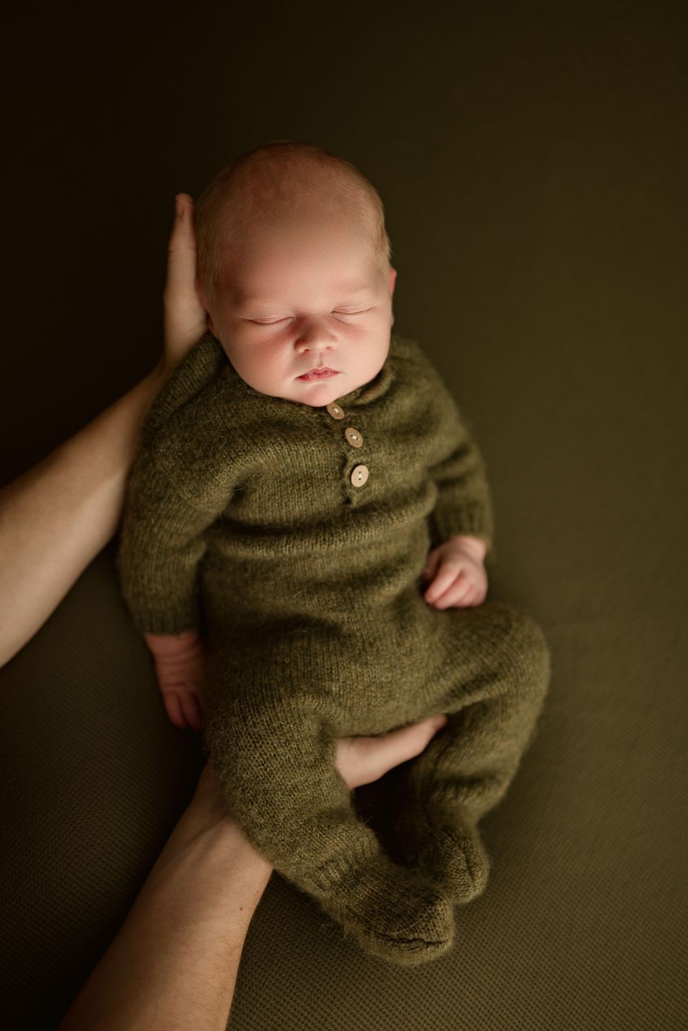 Newborn baby boy sleeps in mom's arms with olive green knit outfit during studio newborn session in Clarksville, Tennessee.