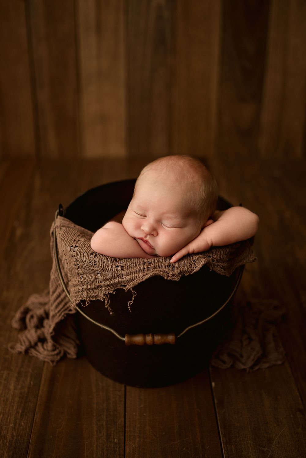 Newborn baby boy sleeps peacefully in bucket during studio newborn session in Clarksville, Tennessee.