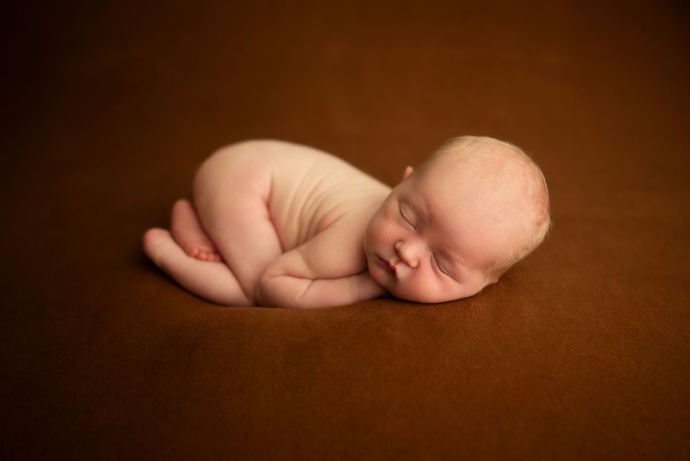 Newborn baby boy with sleeps peacefully on brown backdrop during studio newborn session in Clarksville, Tennessee.